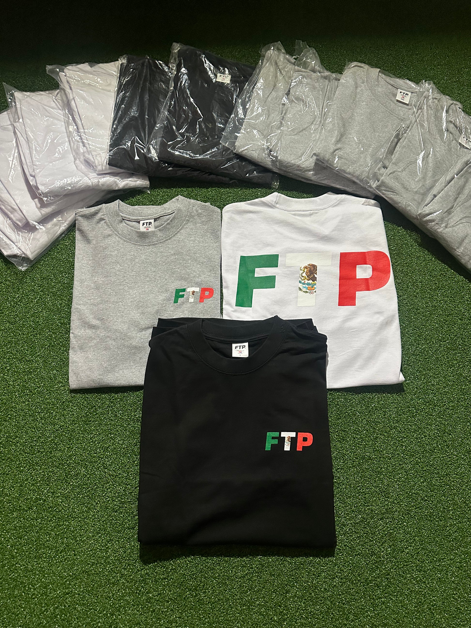 Collection of t-shirts with 'FTP' logo on a green surface