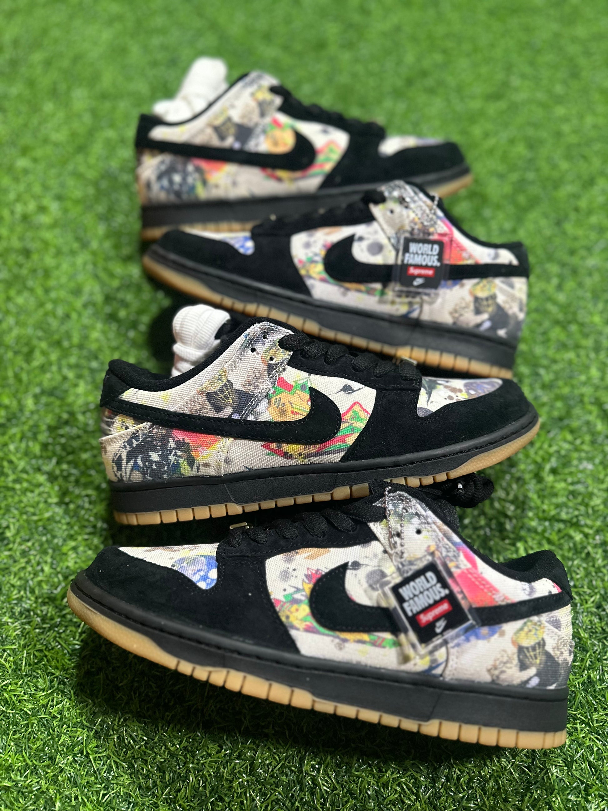 A pair of Nike SB Dunk Low Supreme Rammellzee sneakers with a multicolor design featuring floral patterns and branding on a grass-like surface.