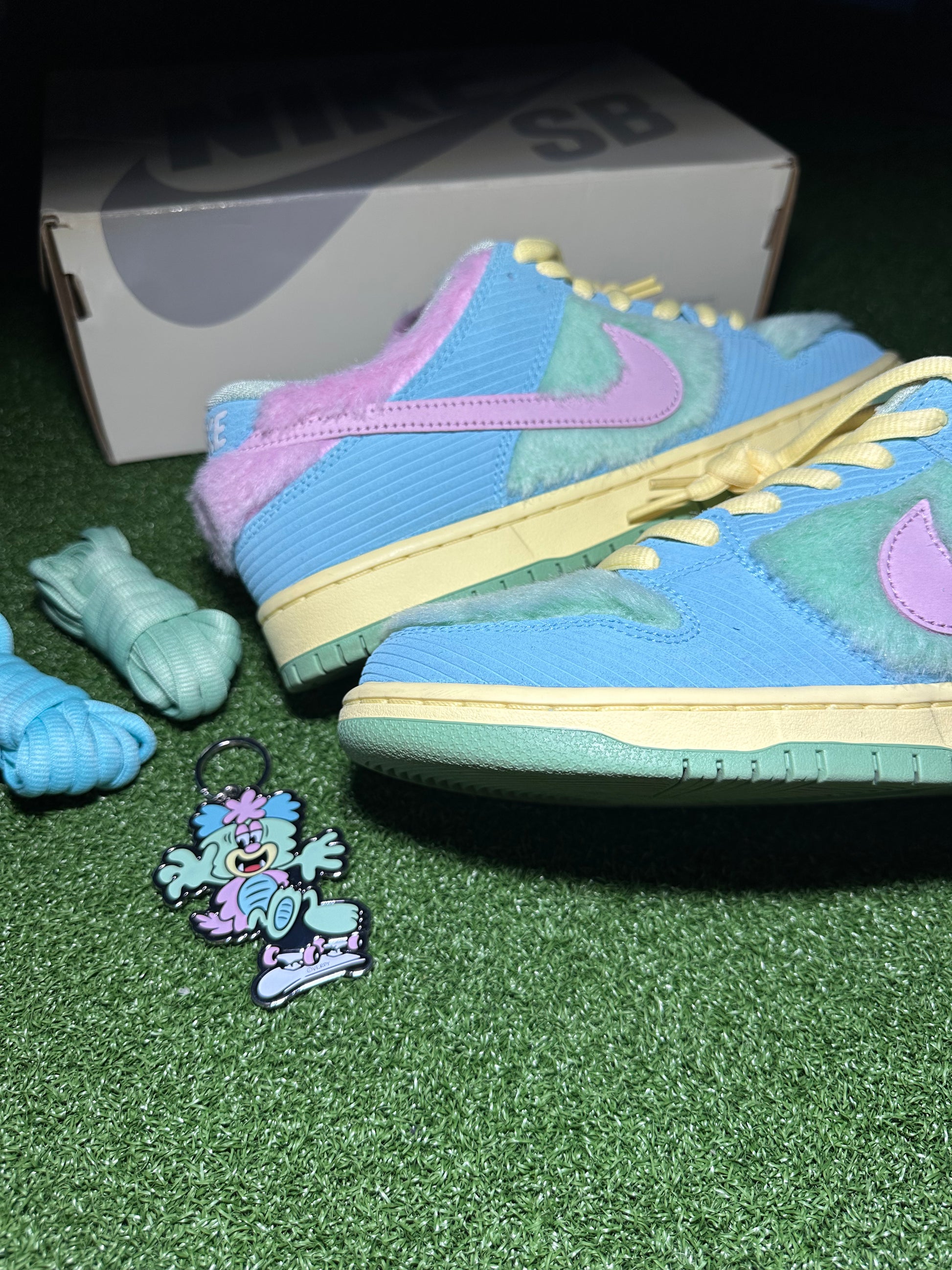 Colorful sneakers with a matching keychain on a green surface, with a Nike SB box in the background.