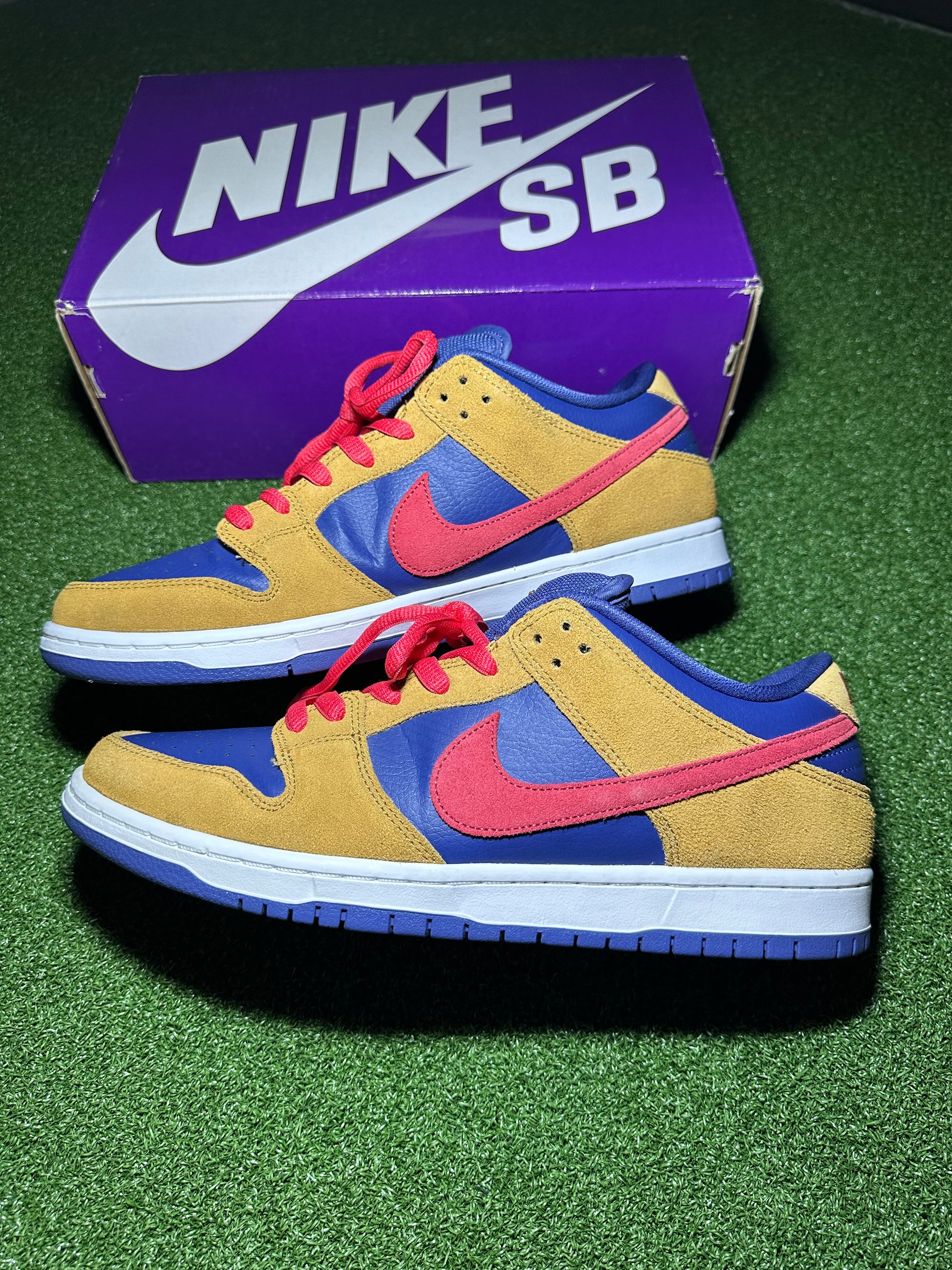 Pair of Nike SB sneakers with a purple box in the background on a green surface