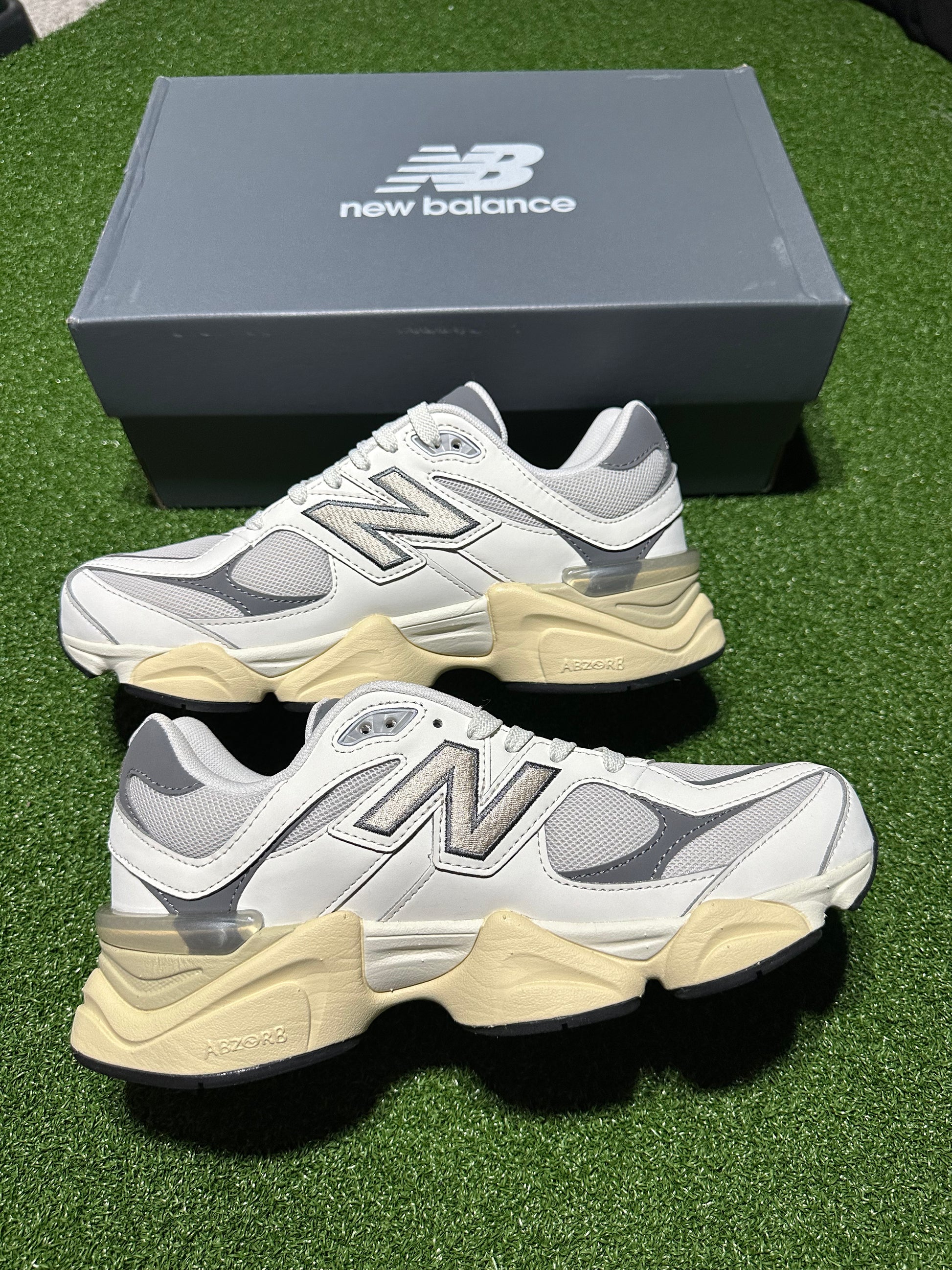 White and beige New Balance sneakers with a matching box on a green surface