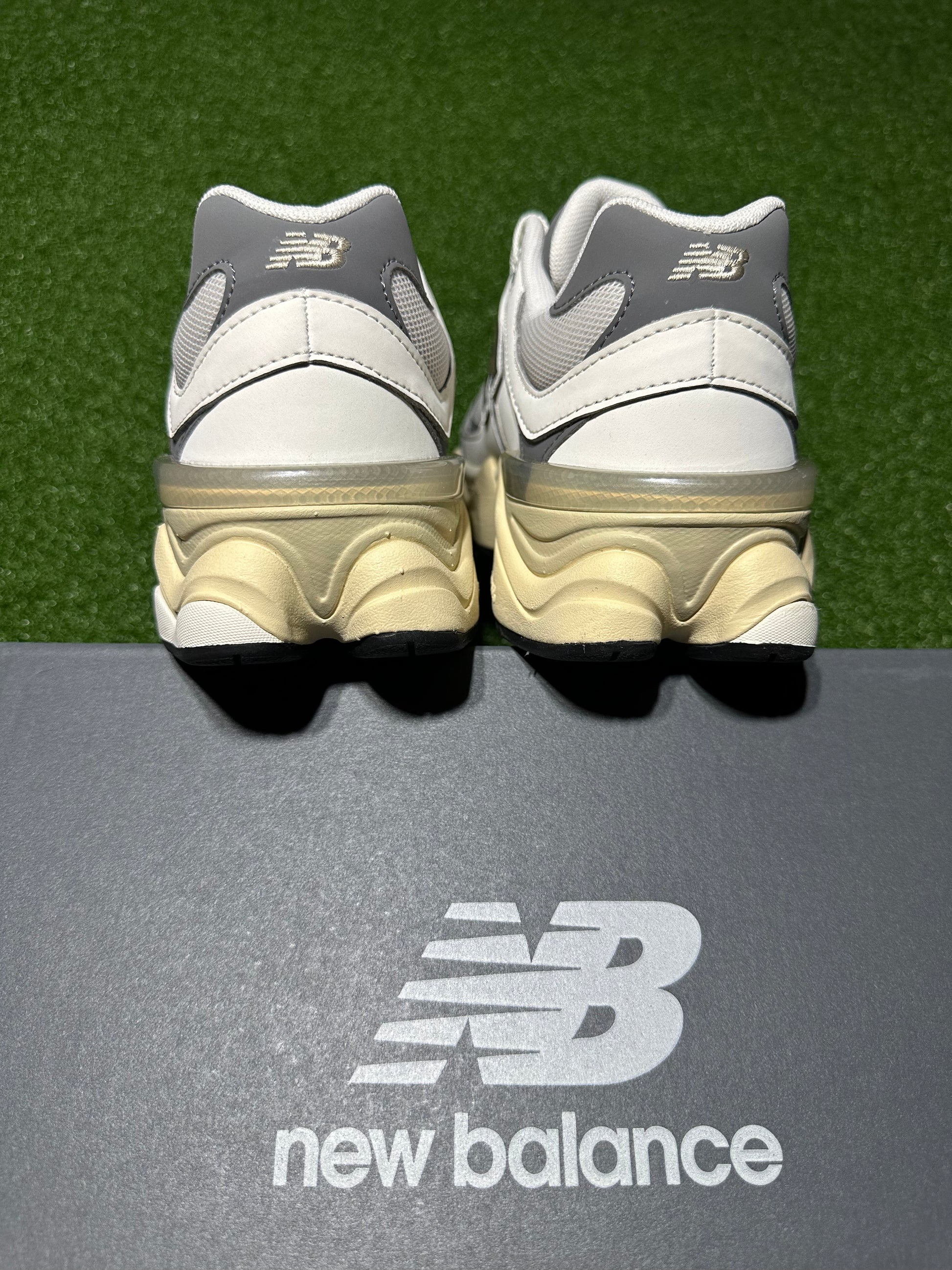 White and gray New Balance sneakers on a gray surface with grass in the background