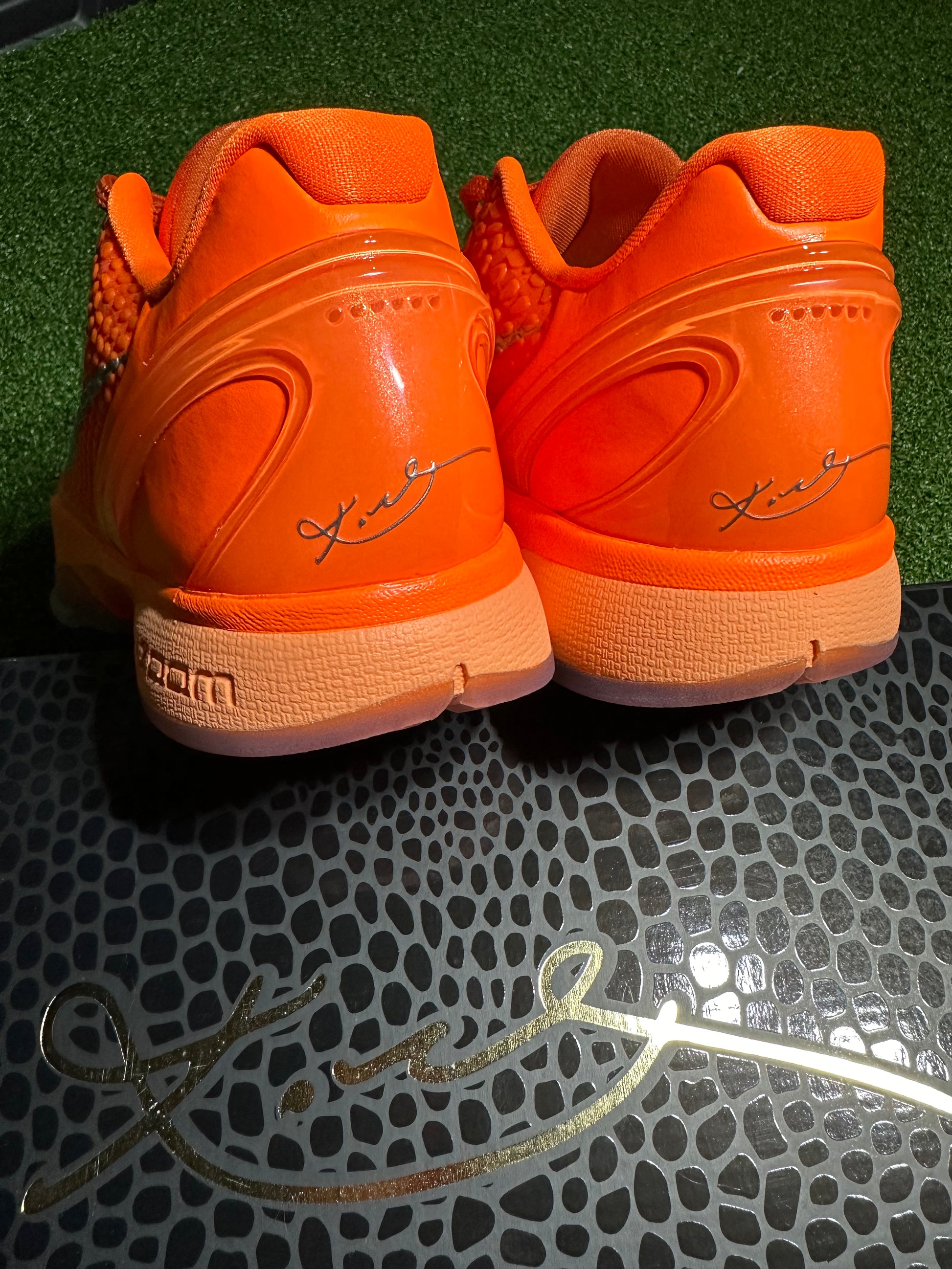 Pair of orange sneakers with a signature on a textured surface