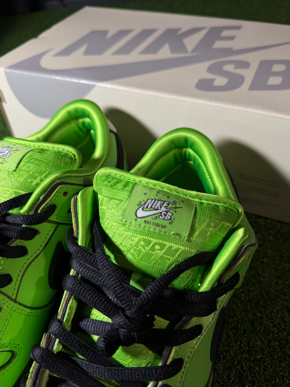 A pair of Nike SB high-top sneakers in a bright neon green colorway with black laces, shown next to their white Nike box.