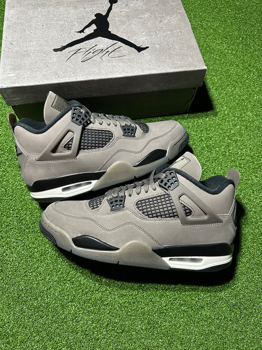 Pair of gray sneakers with black accents on a green surface, with a Jordan box in the background.